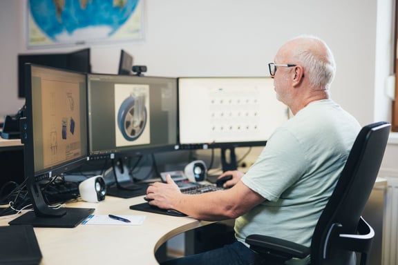 Experte in der technischen Entwicklung am Arbeitsplatz mit mehreren Monitoren – Nutzung des Schwalb Produktkonfigurators für individuelle Räder- und Rollenlösunge